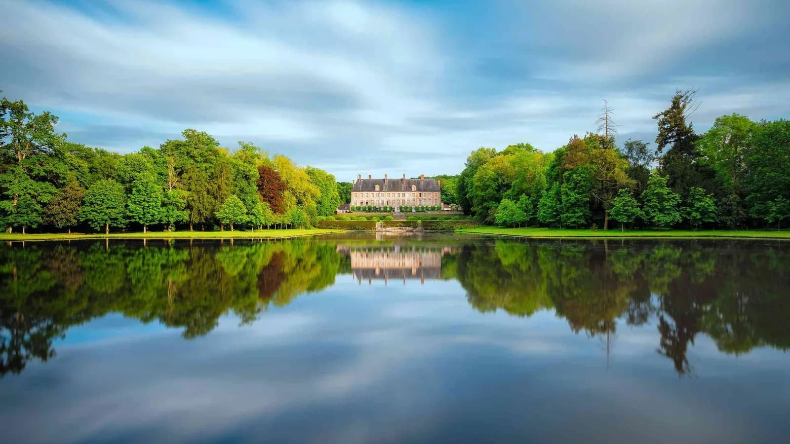 Château reflété dans un lac calme sous un ciel nuageux au Château des Grandes Perspectives, Yvelines