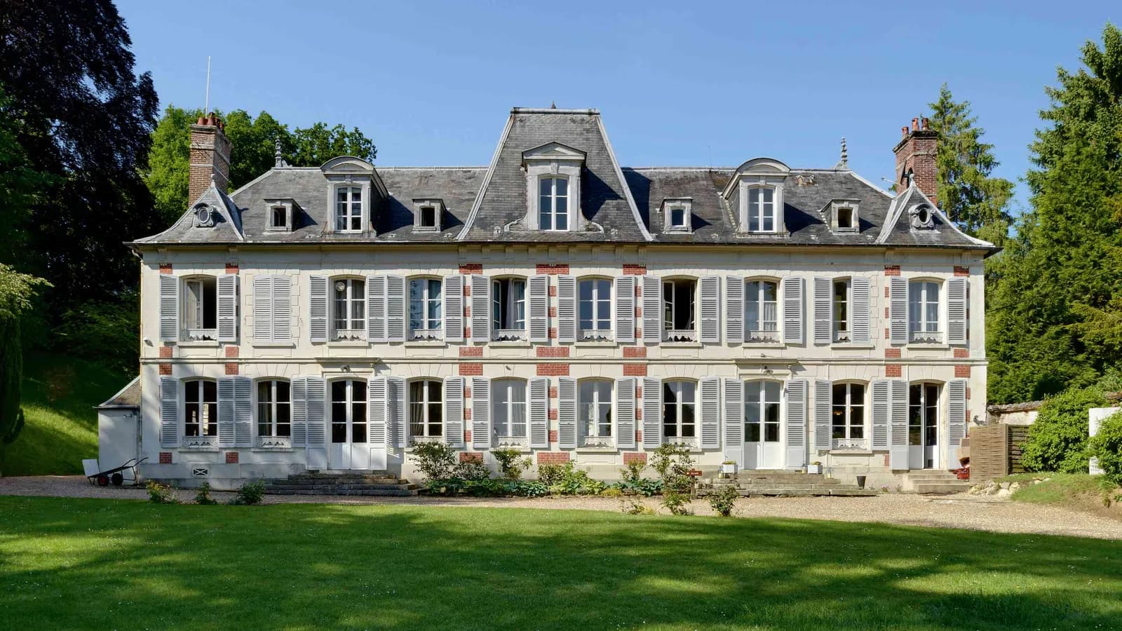 Façade de pierre grise du château, lucarnes et grande pelouse au Château des Lauriers Champêtres, Eure