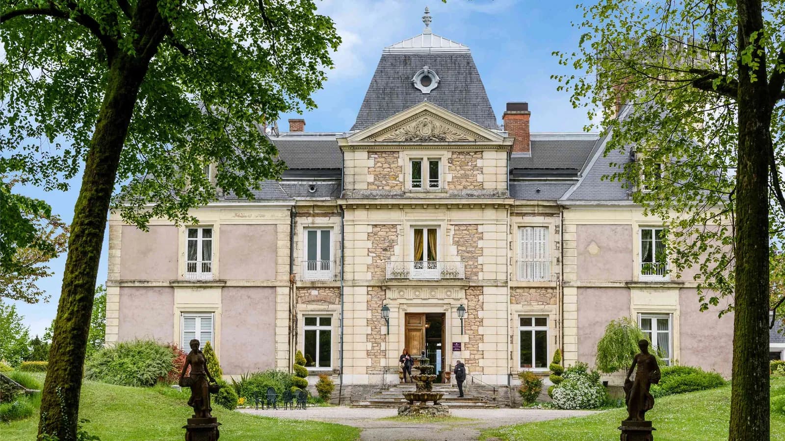 Façade du château encadrée de grands arbres au Château des Quatre Vents, Isère, à l'est de Lyon