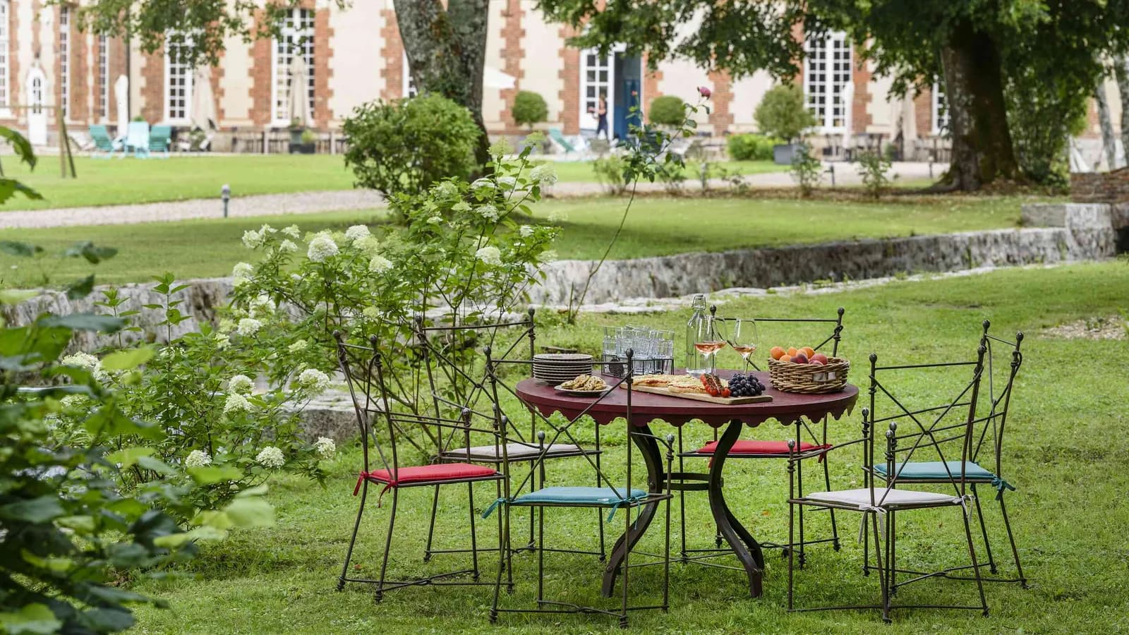 Terrasse de jardin, table et chaises en fer forgé devant la demeure en briques des Pommiers Roses