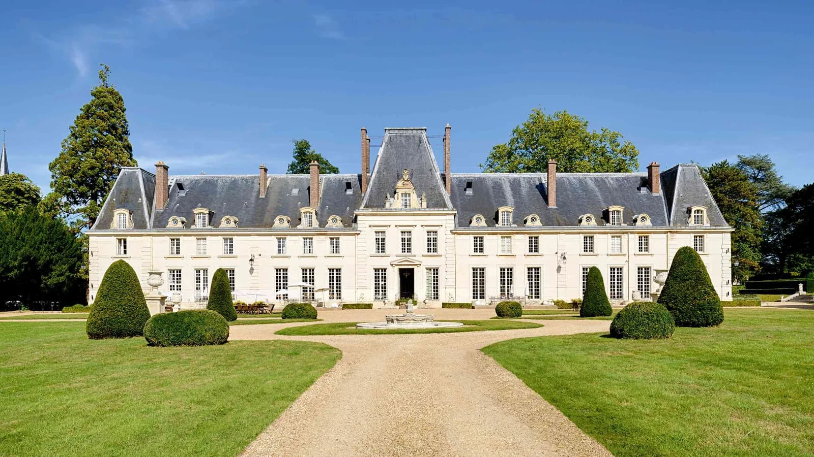 Façade de château sur une pelouse soignée et topiaires taillés au Domaine de la Cour Verte, à l'ouest de Paris