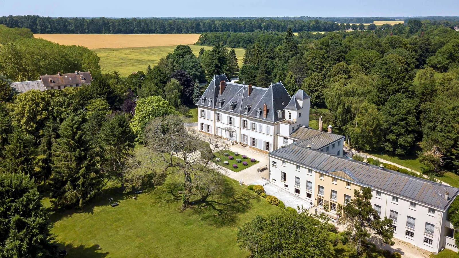 Vue aérienne du Domaine des Herbes Folles, château et ses ailes entourés de jardins, en Seine-et-Marne