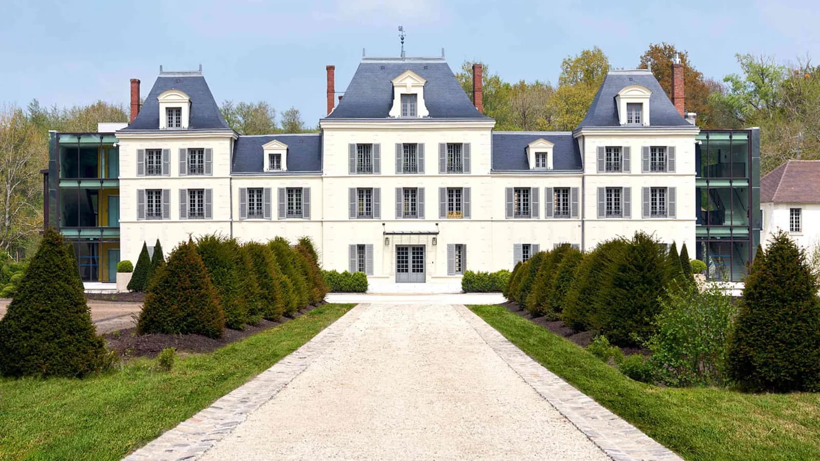 Façade du château et allée de gravier bordée de haies taillées au Domaine des Sources Vertes, dans les Yvelines