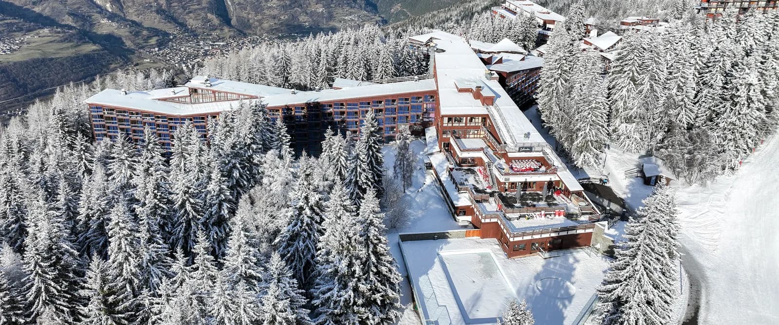Winter aerial view of Hôtel des Cimes d'Argent, a mountain seminar resort in the Tarentaise Alps among snowy pines