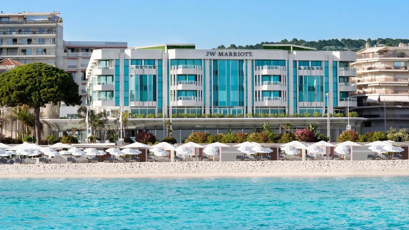Façade du JW Marriott Cannes sur la Croisette, avec piscine turquoise et parasols de plage
