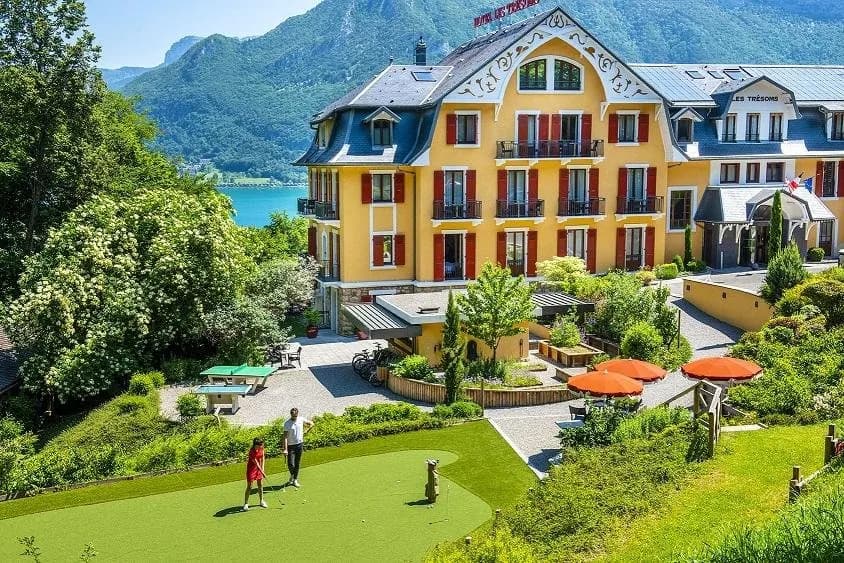 Yellow facade of Les Trésoms Lake and Spa Resort surrounded by gardens above Lake Annecy