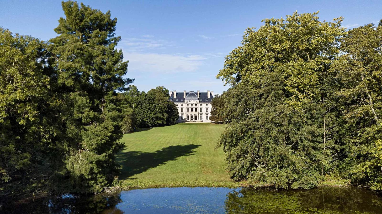 Château entouré de pelouses et d'un étang, sous les arbres, au Manoir des Vallées Claires, Eure-et-Loir