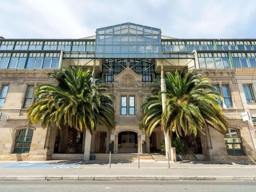 Historic stone facade with palm trees and glass-roofed gallery at Mercure Bordeaux Château Chartrons