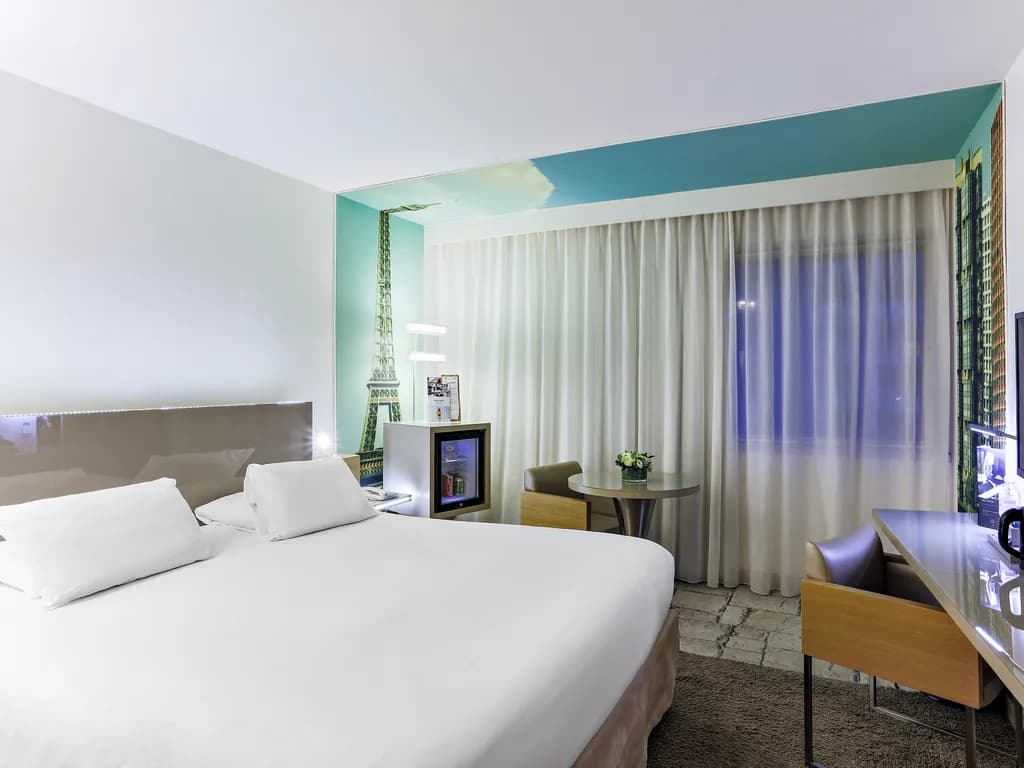 Double room with white bedding, Eiffel Tower wall motif and armchair at Mercure Paris Vaugirard Porte de Versailles