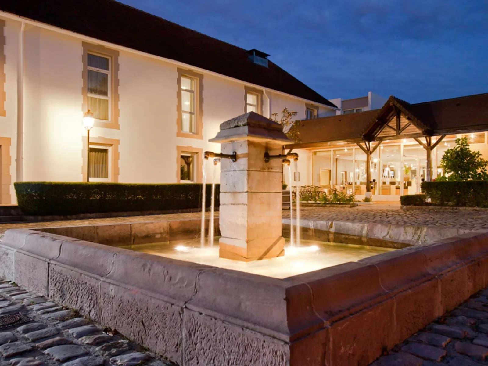 Courtyard fountain and stone entrance of the Novotel Saclay hotel at dusk, Saclay, Essonne