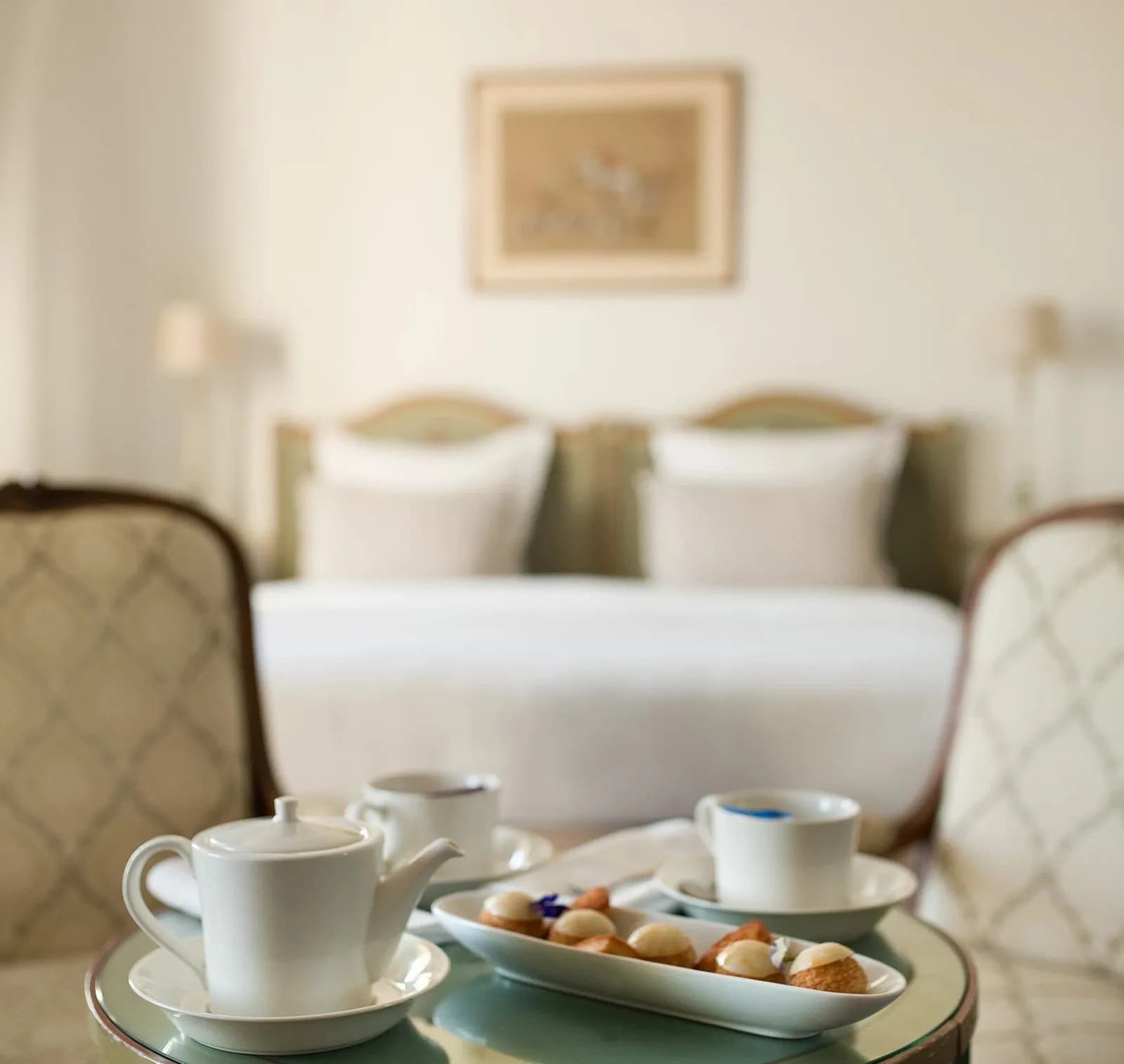 Guest room with cream bedding, antique side table and breakfast tray at Pavillon Henri IV, Saint-Germain-en-Laye
