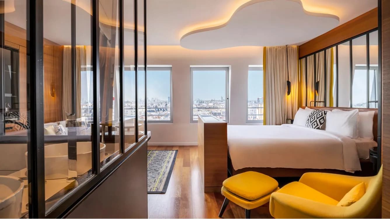 Guest room with glass partition, yellow armchairs and Paris rooftop view at Renaissance Paris République Hotel