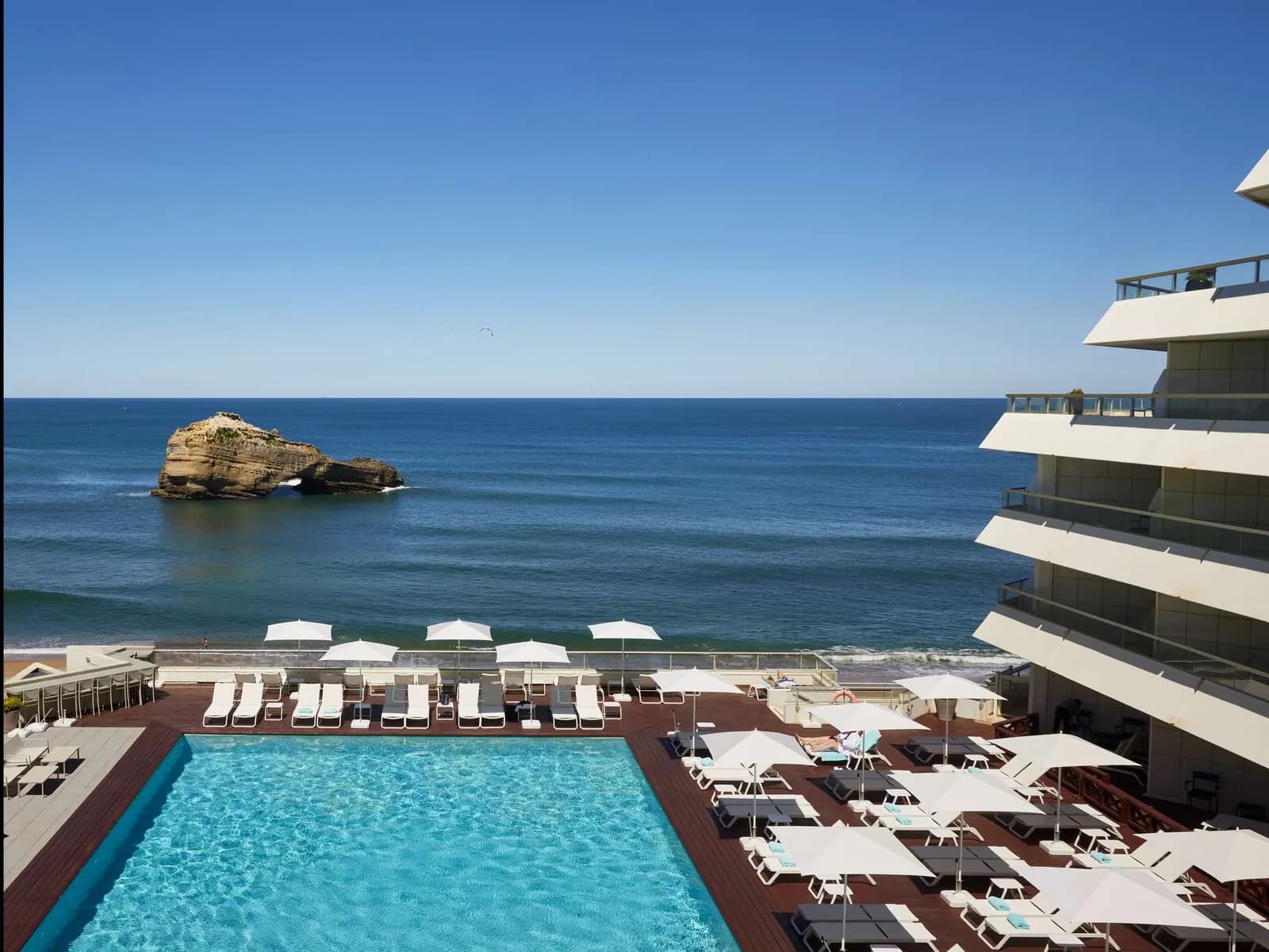 Heated seawater pool with loungers and white parasols facing the ocean at Sofitel Biarritz Le Miramar