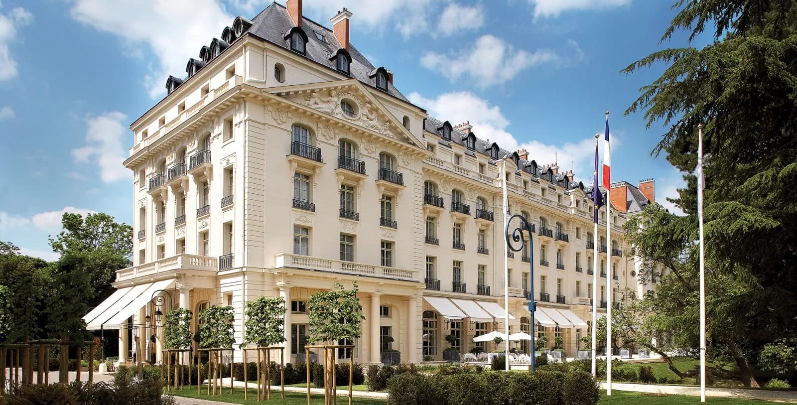 Historic palace facade with French flags and clipped trees at Waldorf Astoria Versailles - Trianon Palace