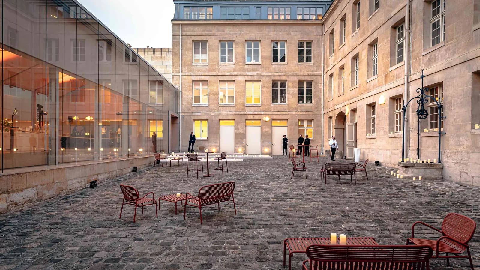 Cour de l'Atrium Rive Gauche avec chaises de jardin rouges et façade en pierre au crépuscule