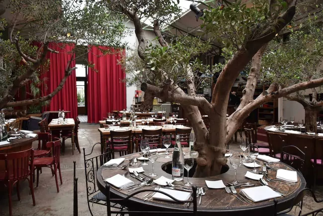 Espace industriel à toiture vitrée, oliviers et tables rondes