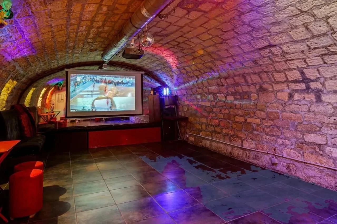 Vaulted stone cellar with a projection screen and red stools