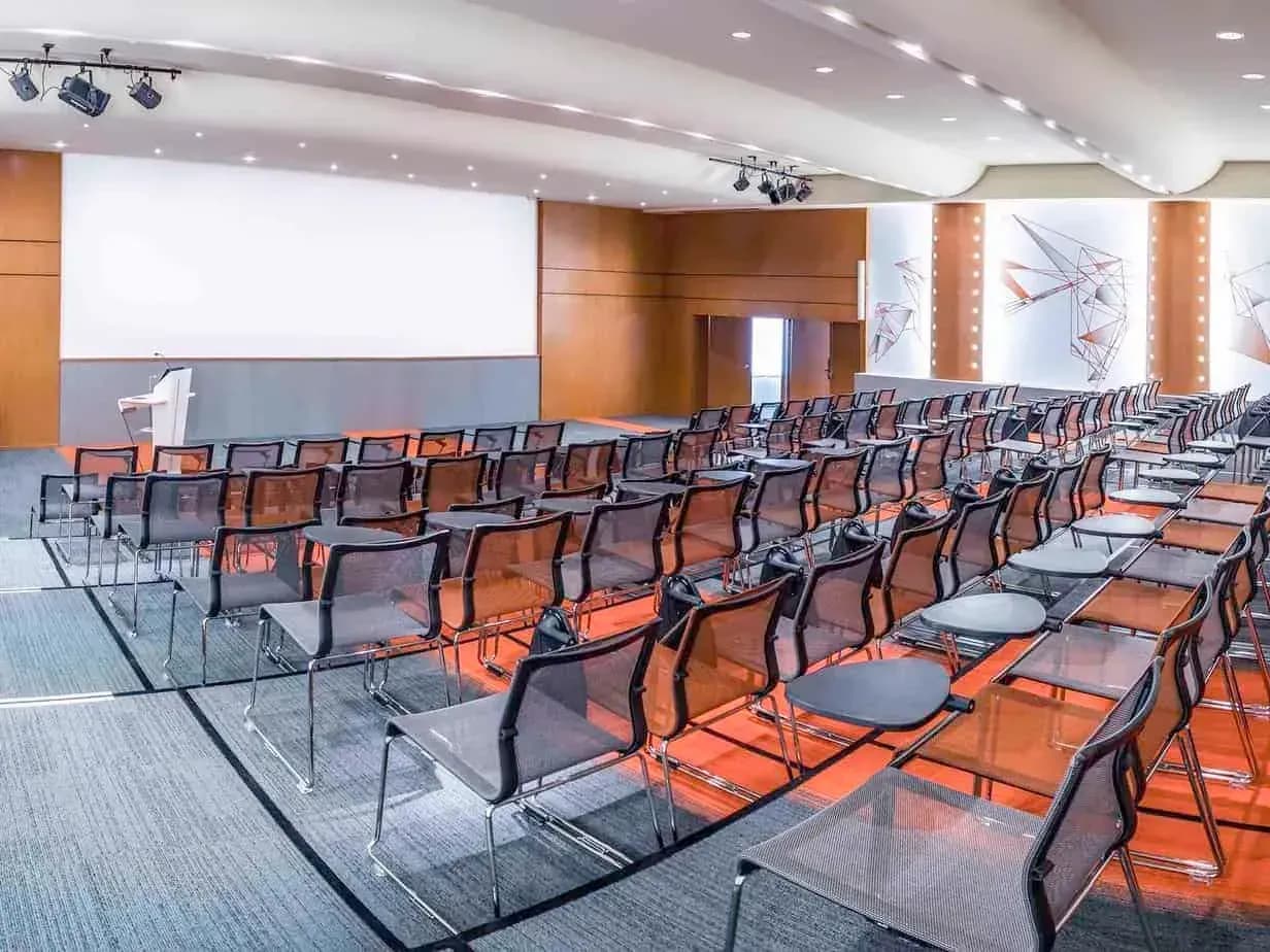 Auditorium with rows of mesh chairs, timber wall panels and a large screen