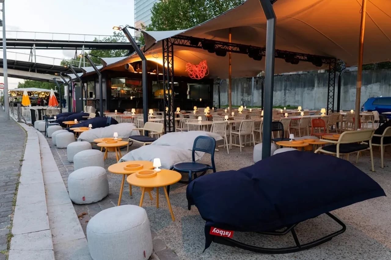 Riverside terrace with bean-bag seating, round tables and a canopy over a dining area.