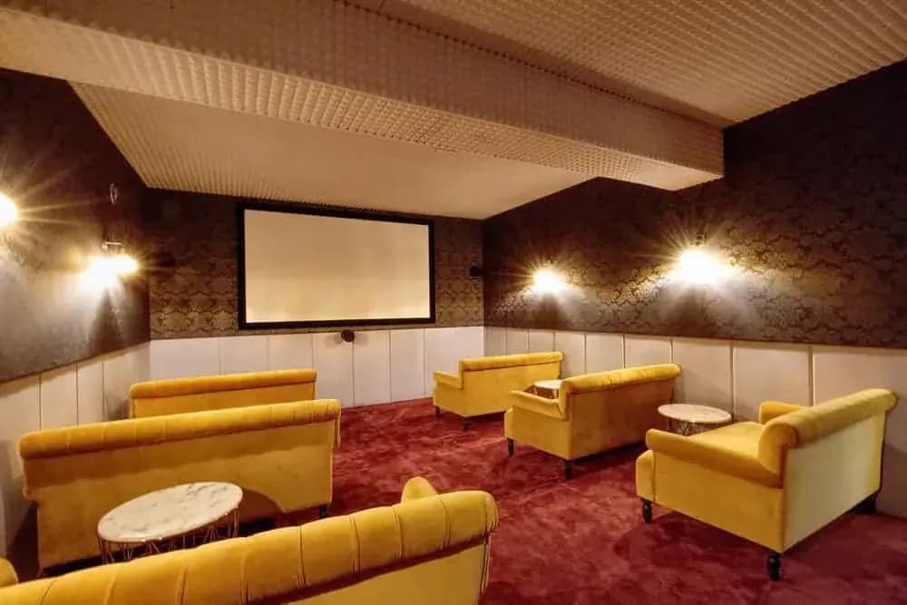 Private cinema room with yellow velvet armchairs, a wall screen and red carpet