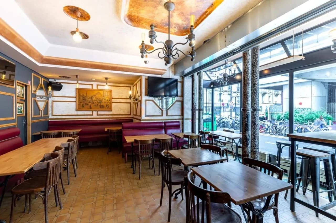 Bistro dining room with wood tables, booth seating and a chandelier beside a street window.