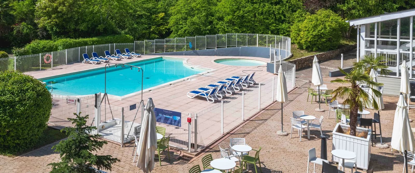 Outdoor pool and sunny terrace framed by tall trees at Domaine des Rives de l'Orge, a wooded seminar resort in Essonne