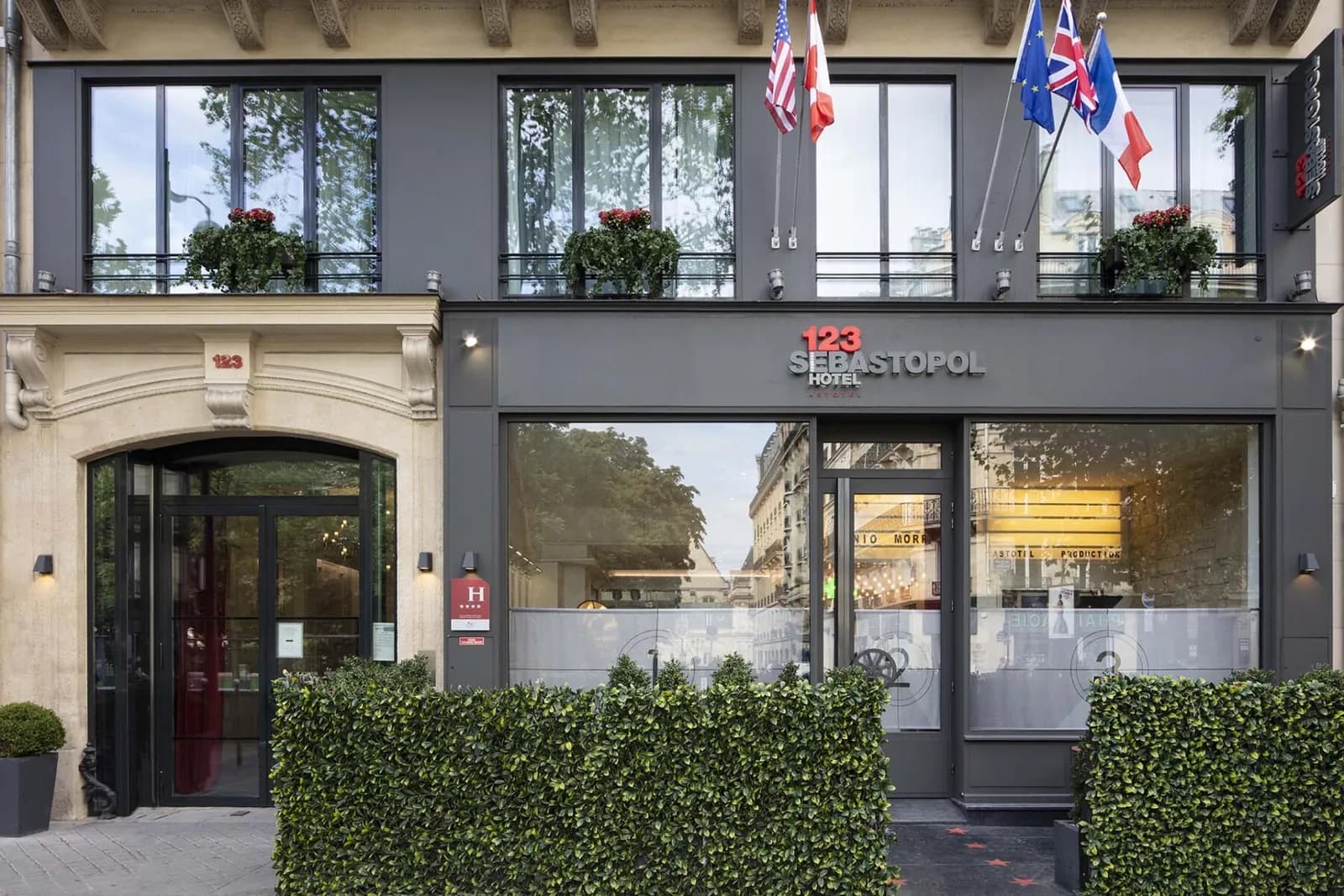 Grey-fronted facade of the 123 Sébastopol hotel on Boulevard de Sébastopol, with national flags and hedges