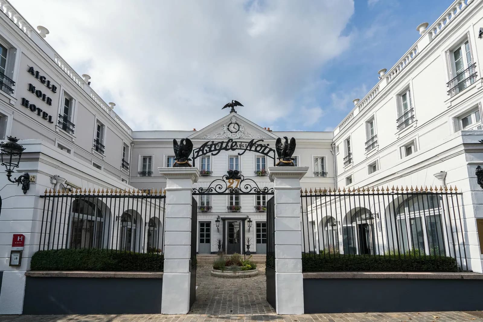White stone facade and wrought-iron gates of the MGallery Aigle Noir hotel in Fontainebleau, near the palace