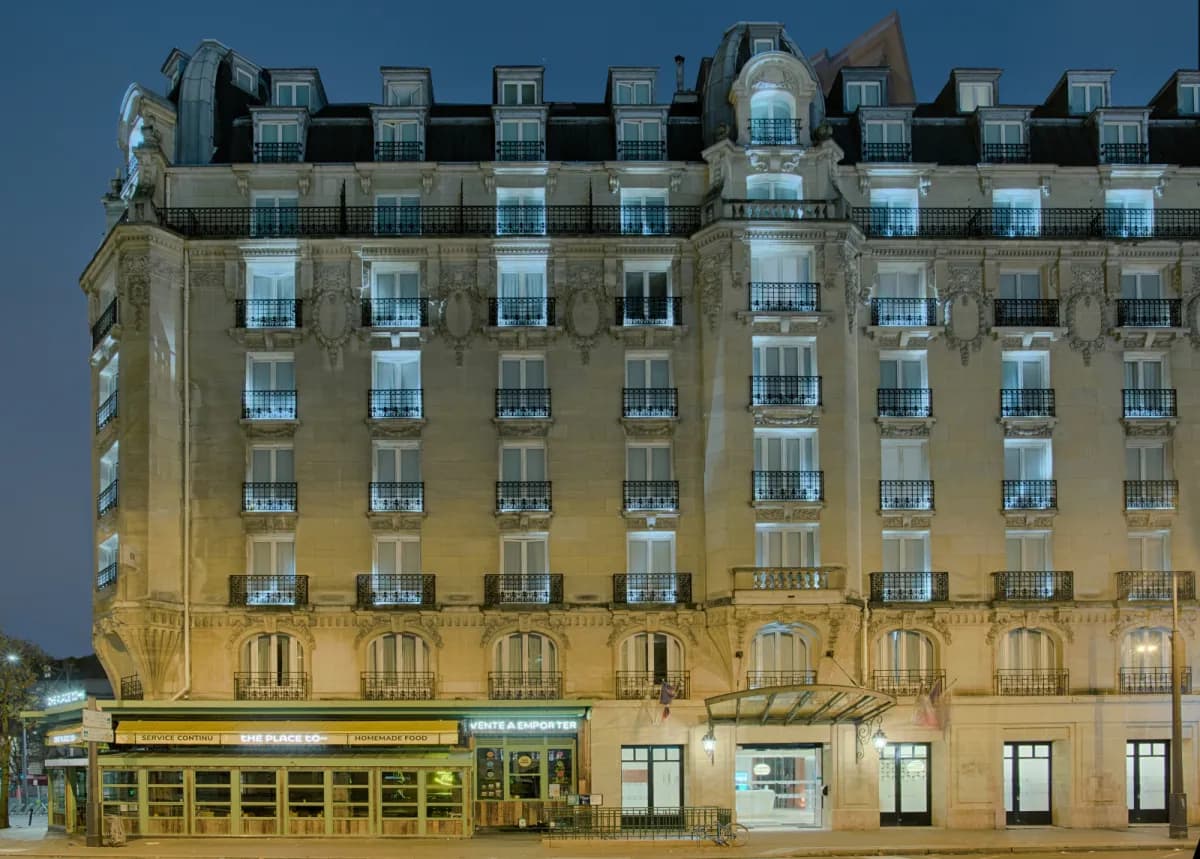 Façade du NH Paris Gare de l'Est au crépuscule, immeuble en pierre de style haussmannien aux fenêtres éclairées