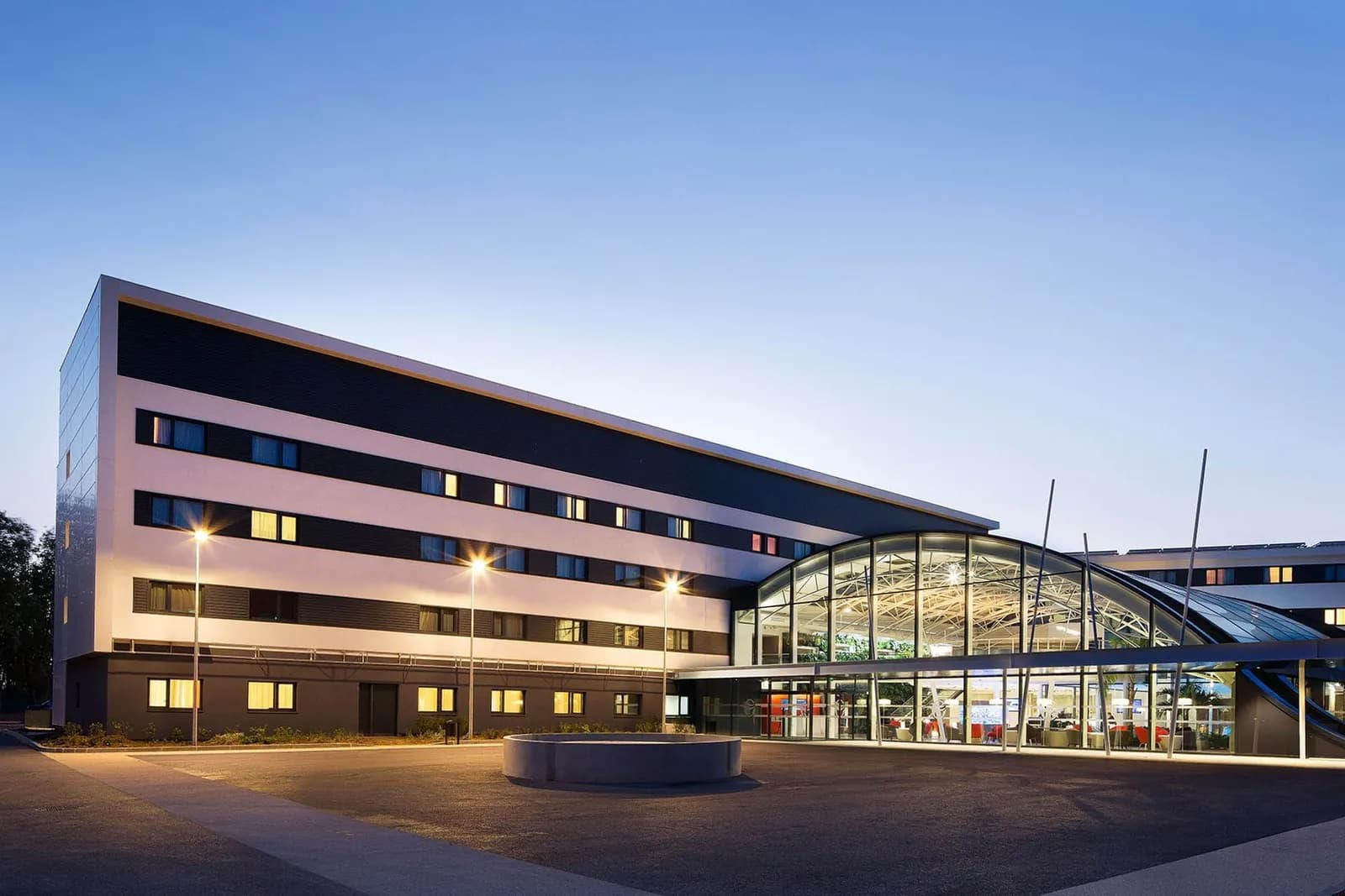 Exterior of Oceania Paris Roissy CDG at dusk, with its glass-roofed entrance and lit facade