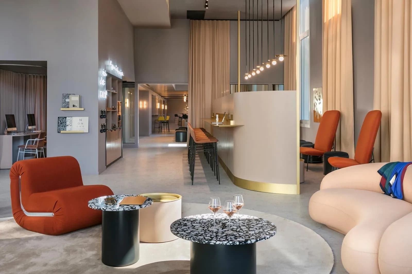 Lounge of the OKKO Hotels Paris Gare de l'Est with orange armchairs, round side tables and a curved beige reception counter