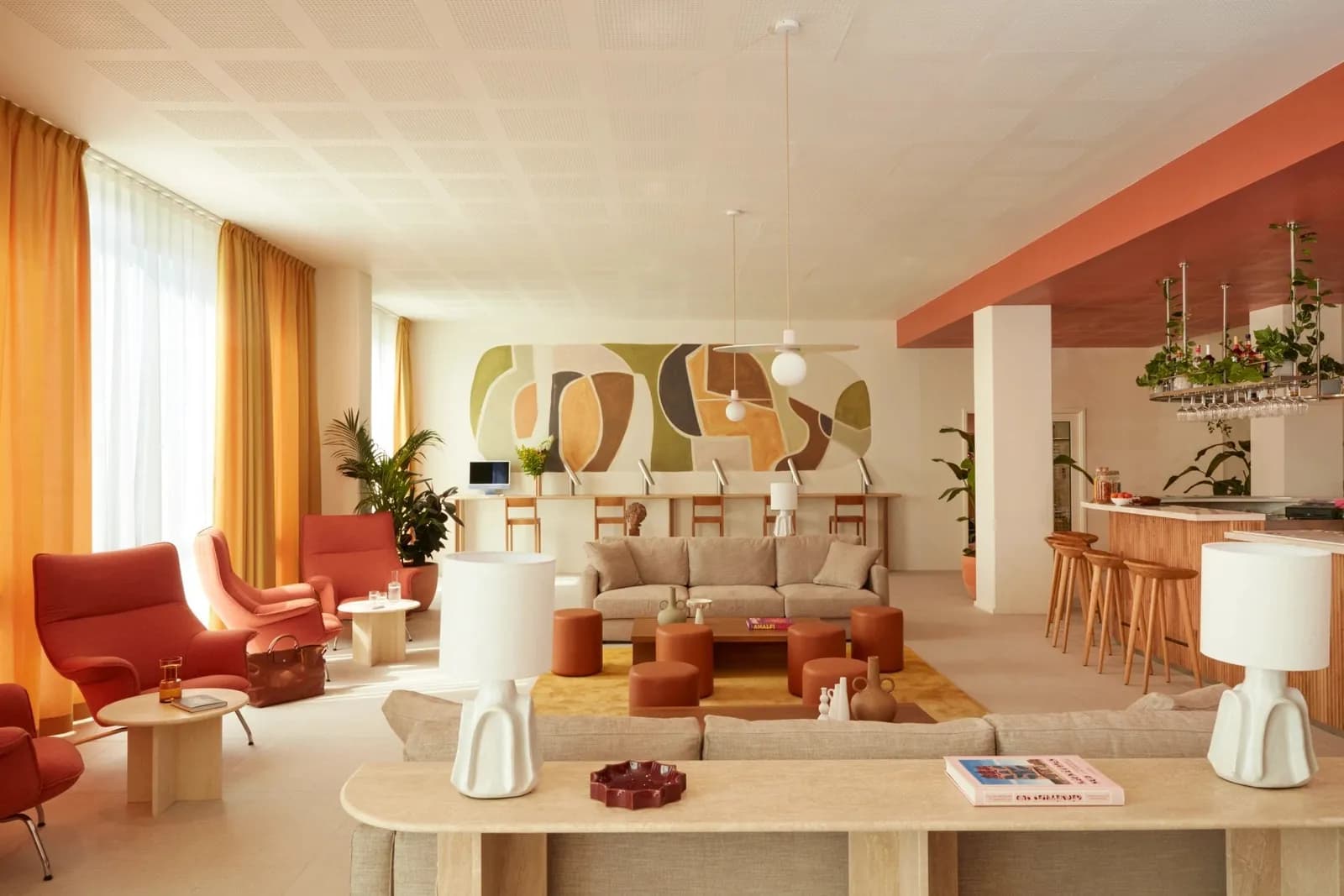 Lounge et bar de l'OKKO Hotels Paris Rosa Parks avec fauteuils rouges, comptoir en bois, tabourets hauts et rideaux chauds