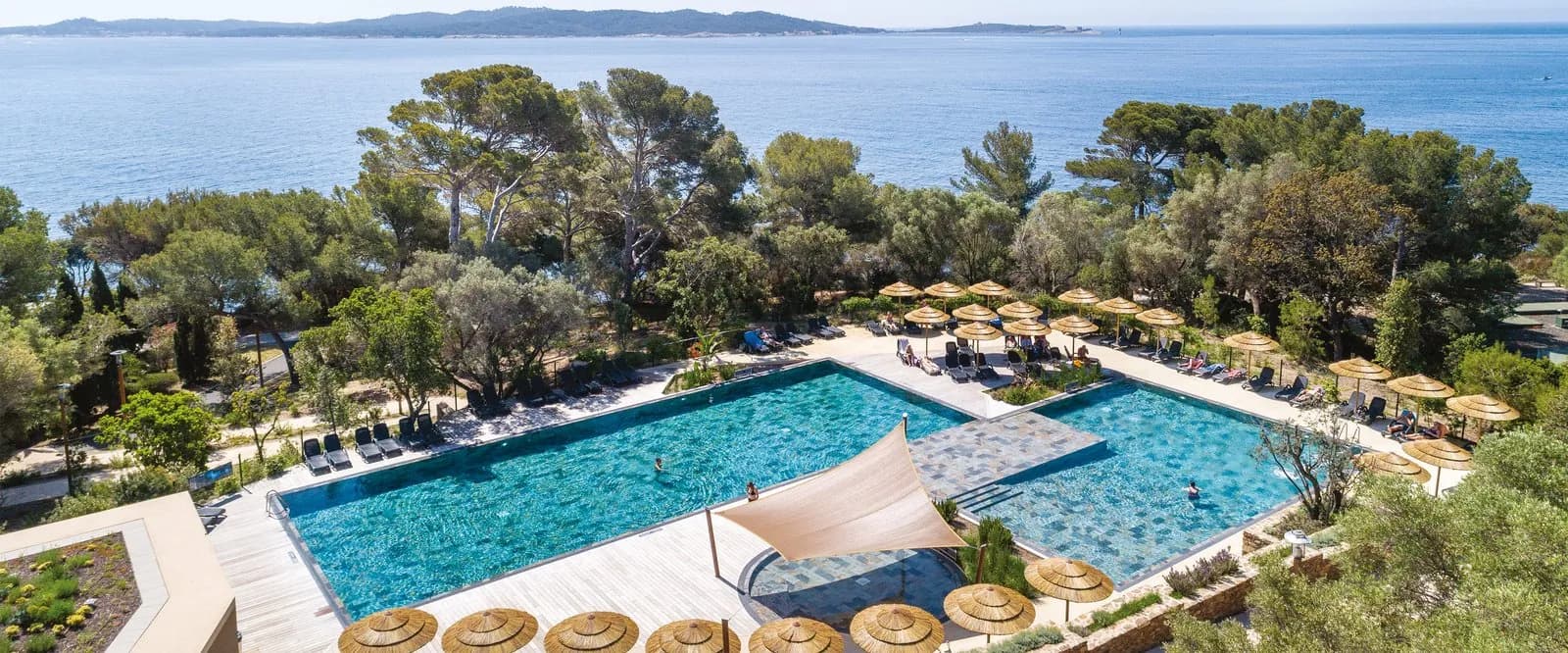 Aerial view of a seaside pool with parasols, pine trees and the Mediterranean at Résidence des Pins Méditerranéens