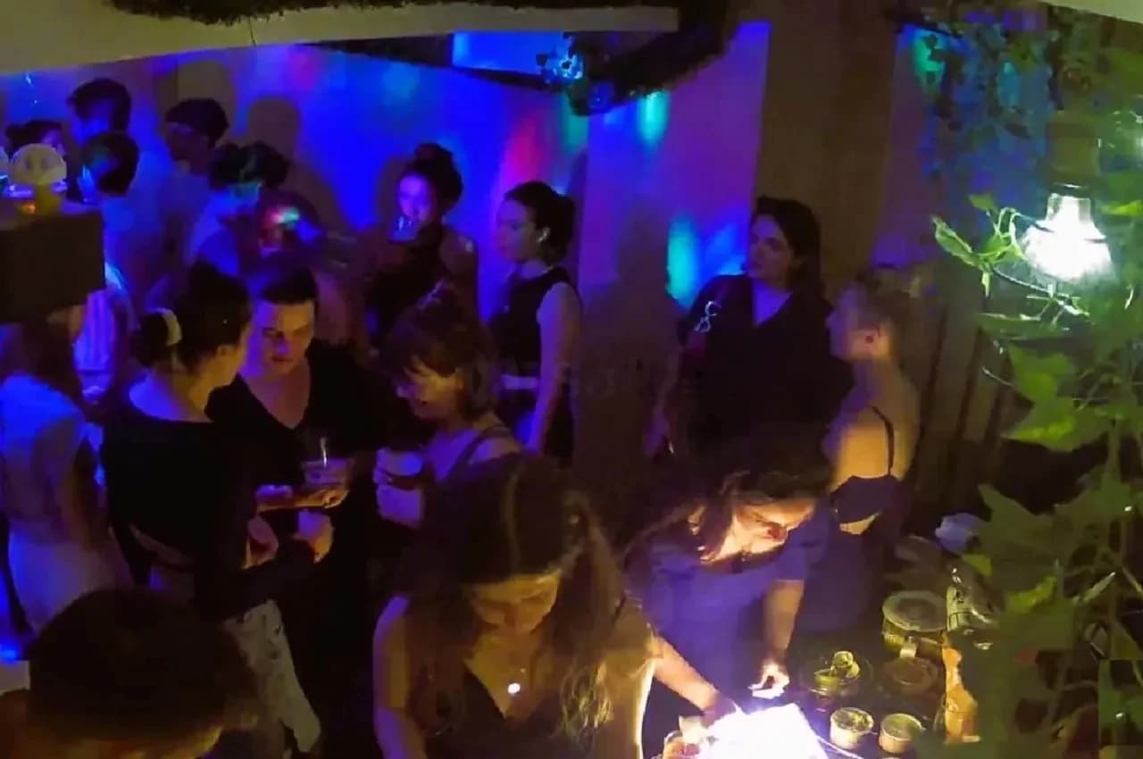 Guests standing at a buffet in a dimly lit room with blue lighting and plants.