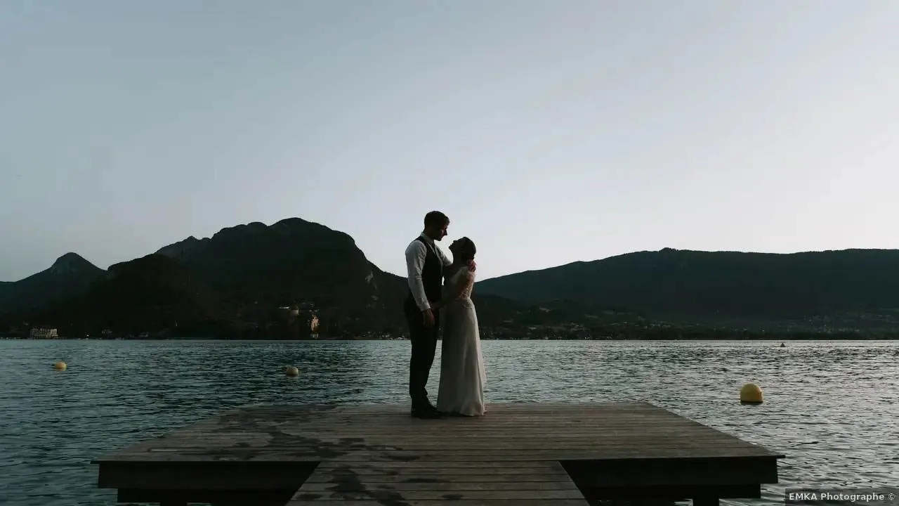Couple on the wooden jetty of L'Abbaye de Talloires with mountains across Lake Annecy