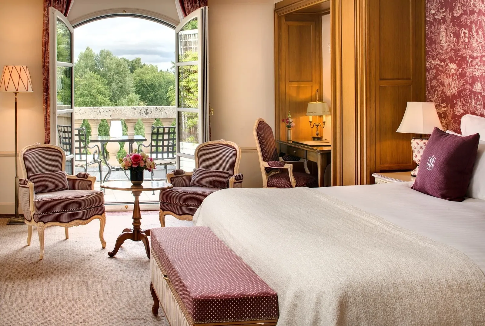 Guest room at the Auberge du Jeu de Paume with a double bed, armchairs and a balcony door opening onto the park