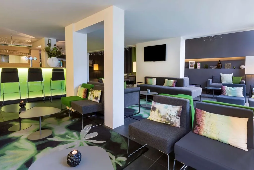 Espace salon de l'hôtel Best Western Plus Hôtel du Parc Chantilly avec canapés gris, tabourets verts et écran plat
