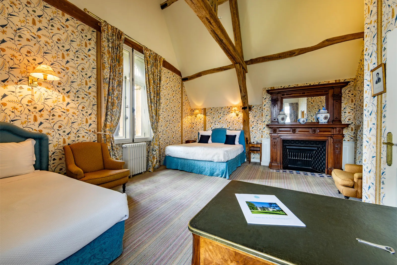 Château guest room with floral wallpaper, fireplace and a blue bed at Château de la Bourdaisière