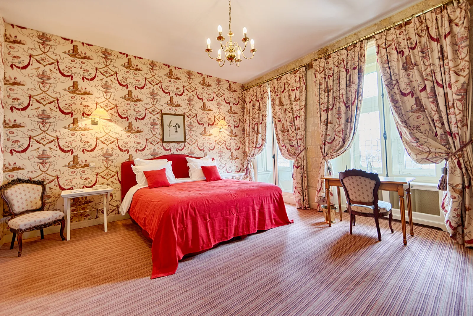 Guest room with red floral wallpaper, red bedspread and tall windows at Château de la Bourdaisière