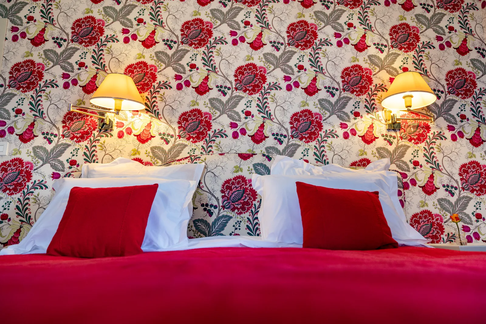 Close-up of a red bed with floral wallpaper and bedside lamps at Château de la Bourdaisière