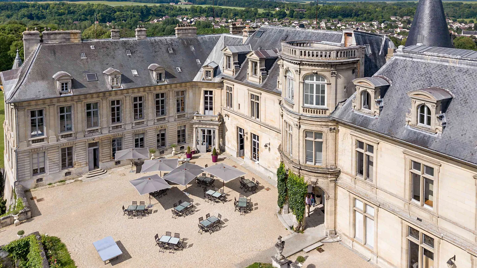 Cour du Château des Tourelles Blanches avec tour ronde, lucarnes et parasols, à l'ombre des grands arbres