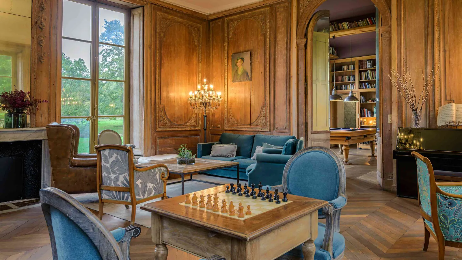 Wood-panelled library lounge with a chess table and blue armchairs at Château du Val Vert, Val-d'Oise