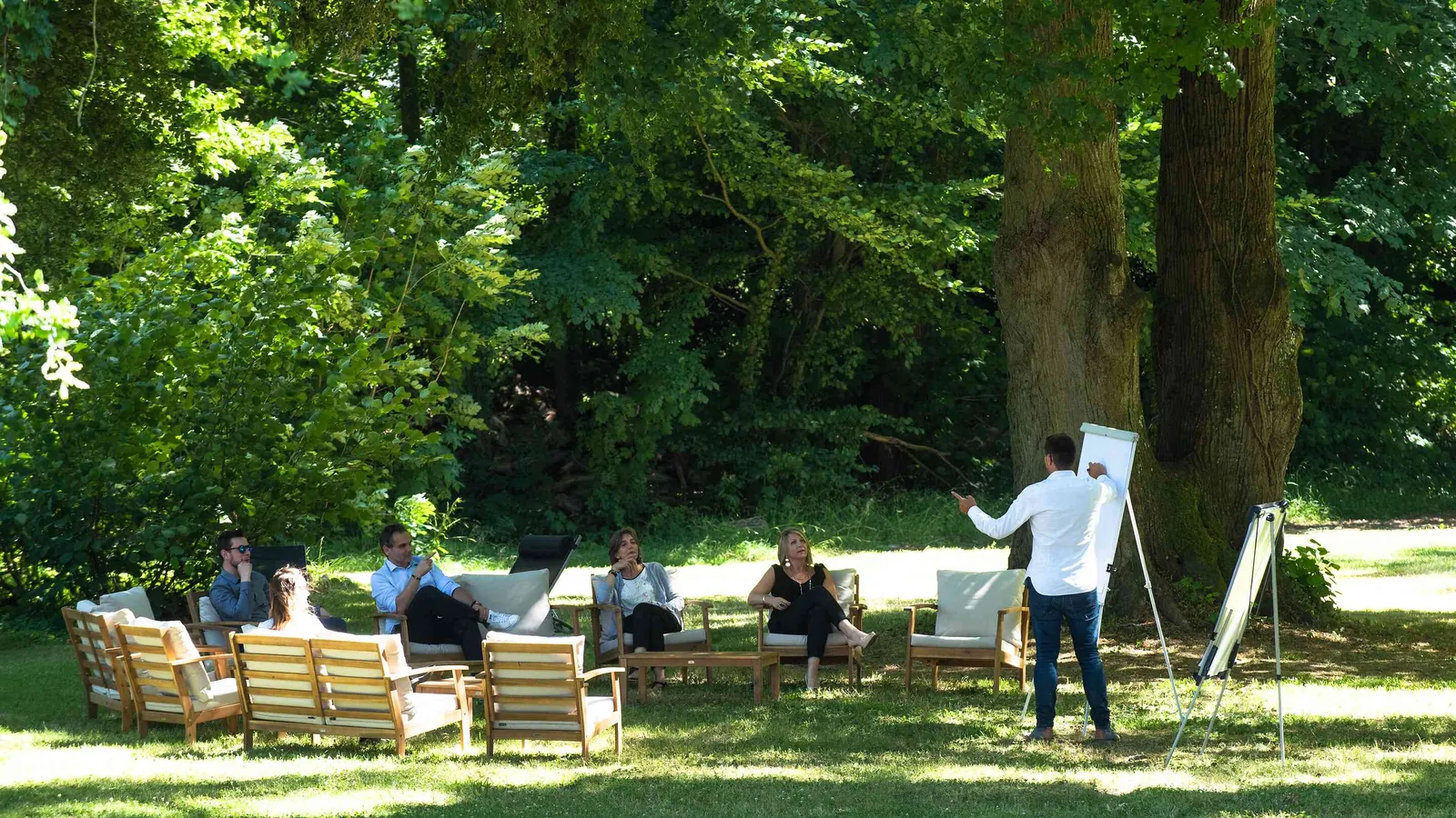 Outdoor seminar session on the lawn under mature trees with a flipchart at Domaine de la Cour Verte