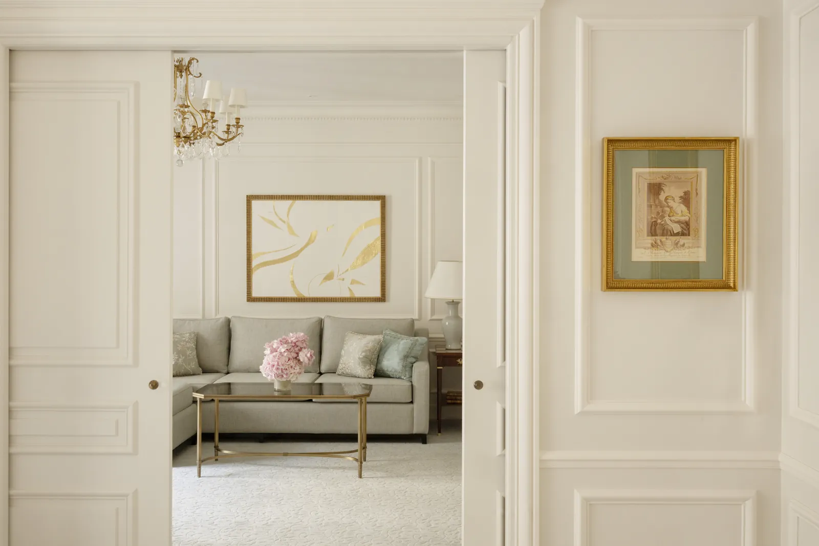 Salon de suite avec canapé crème, œuvre dorée et portes à panneaux au Four Seasons Hotel George V, Paris