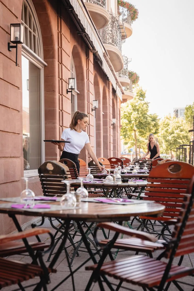 Shaded outdoor terrace with wooden chairs and a waitress at Grand Hôtel Bristol, Colmar