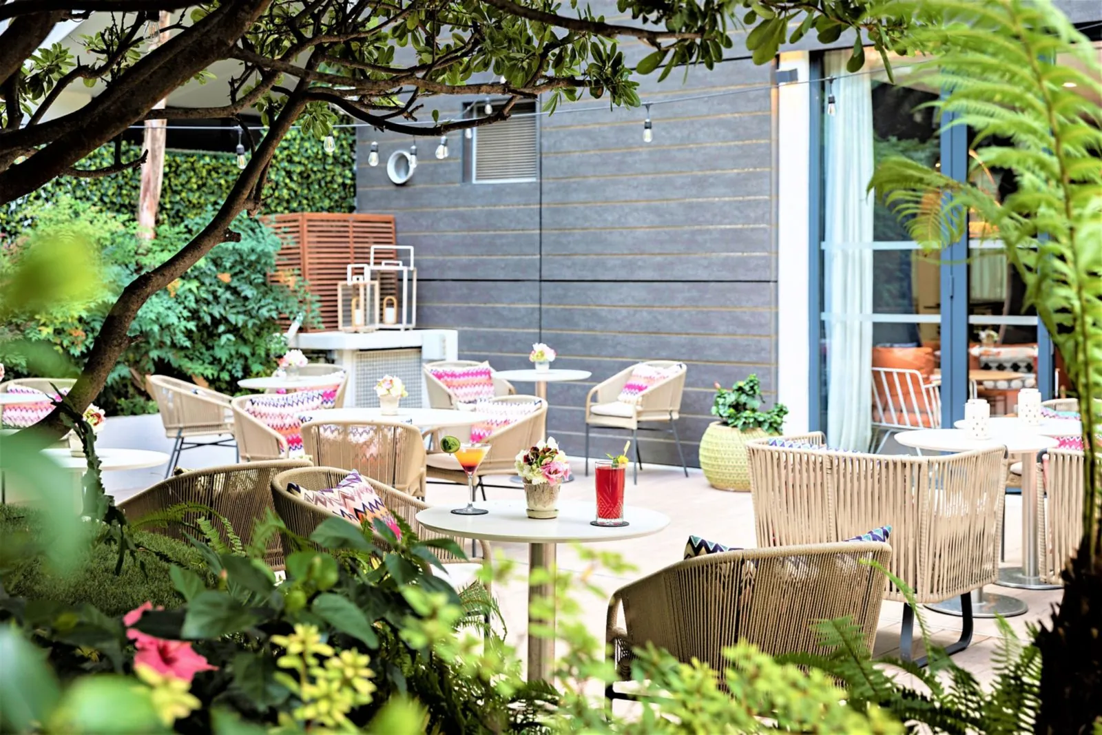 Garden terrace shaded by trees with wicker chairs and tables at Hôtel Croisette Beach Cannes MGallery, Cannes