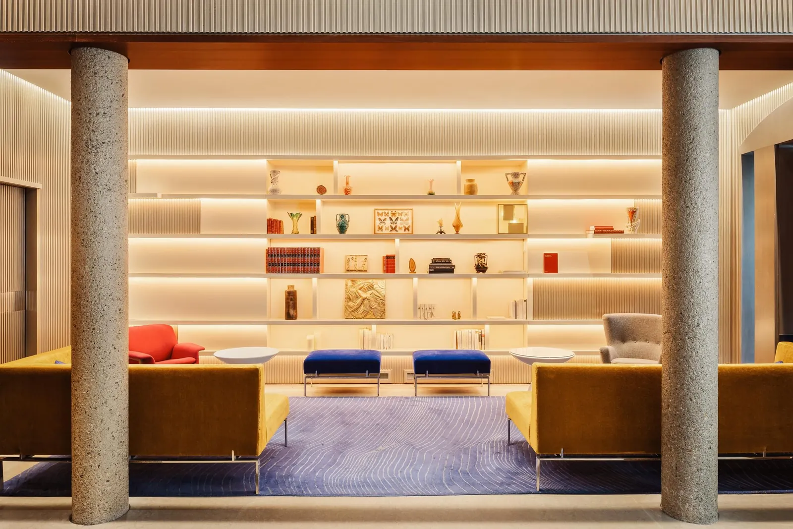 Lobby of Hôtel de Sers in Paris with stone columns, a lit display wall and yellow velvet sofas