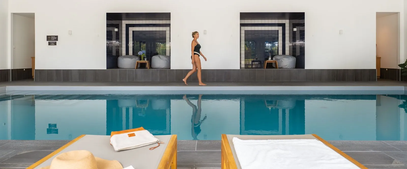 Heated indoor pool with loungers and a guest on the pool deck at Hôtel des Rivages Argentés, Finistère