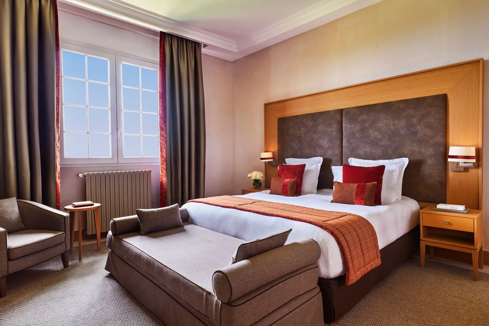 Classic deluxe bedroom with a brown headboard, red cushions and bay window at Hôtel du Golf Barrière, Deauville