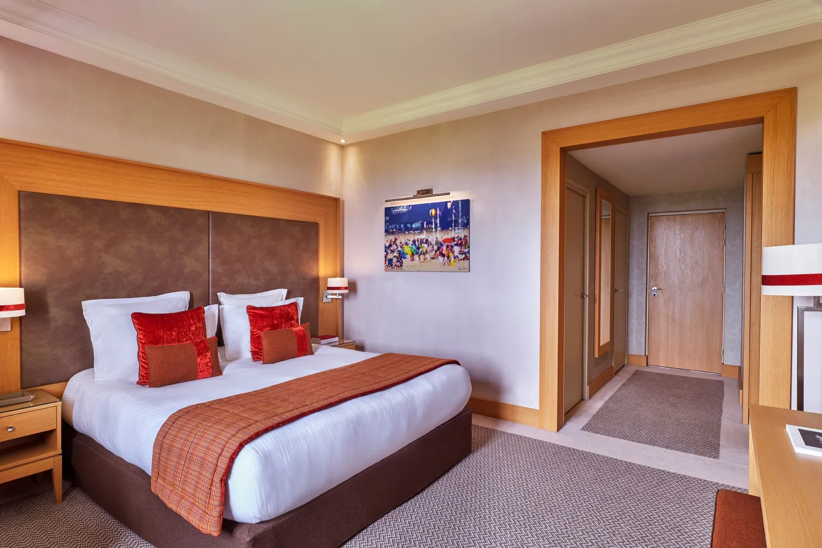 Superior bedroom with a red bedspread, reading armchair and entrance corridor at Hôtel du Golf Barrière, Deauville